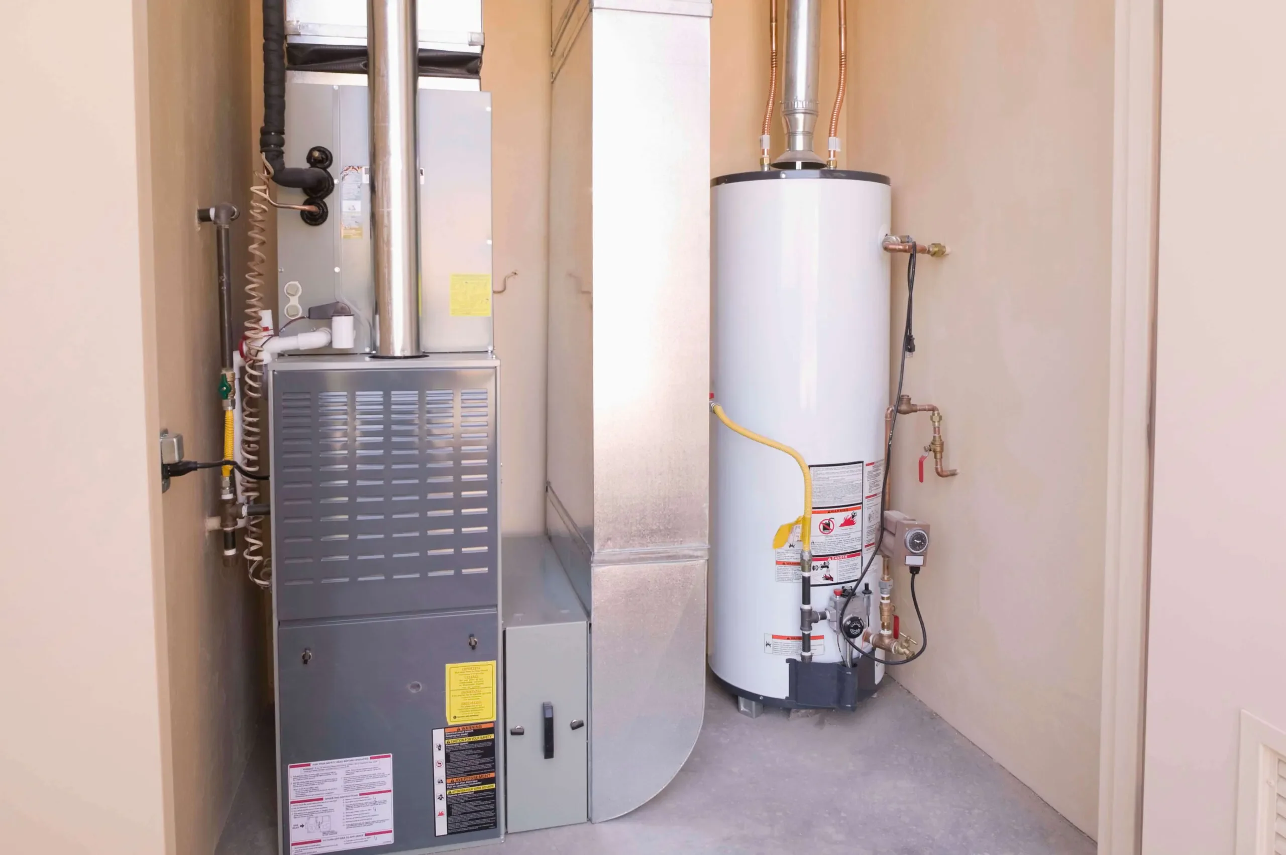 A furnace and a water heater installed side by side in a small utility room with beige walls and concrete flooring—ideal for homes in TX considering ac replacement San Antonio services.