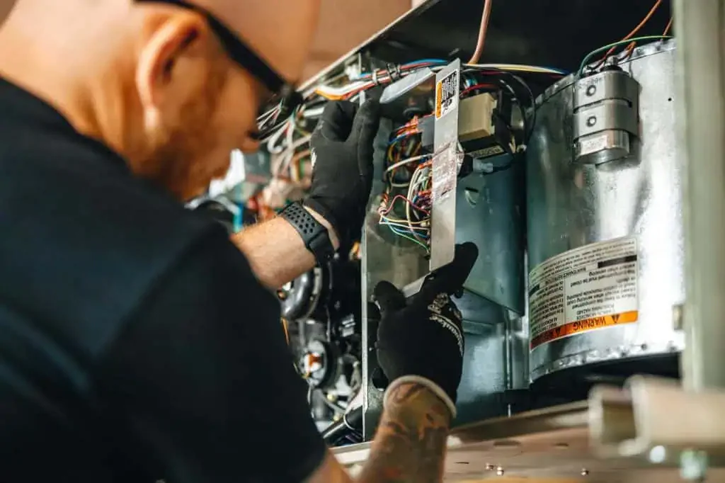 A technician wearing black gloves works on the wiring inside an HVAC unit, using tools to inspect electrical connections as part of an ac replacement in San Antonio, TX.