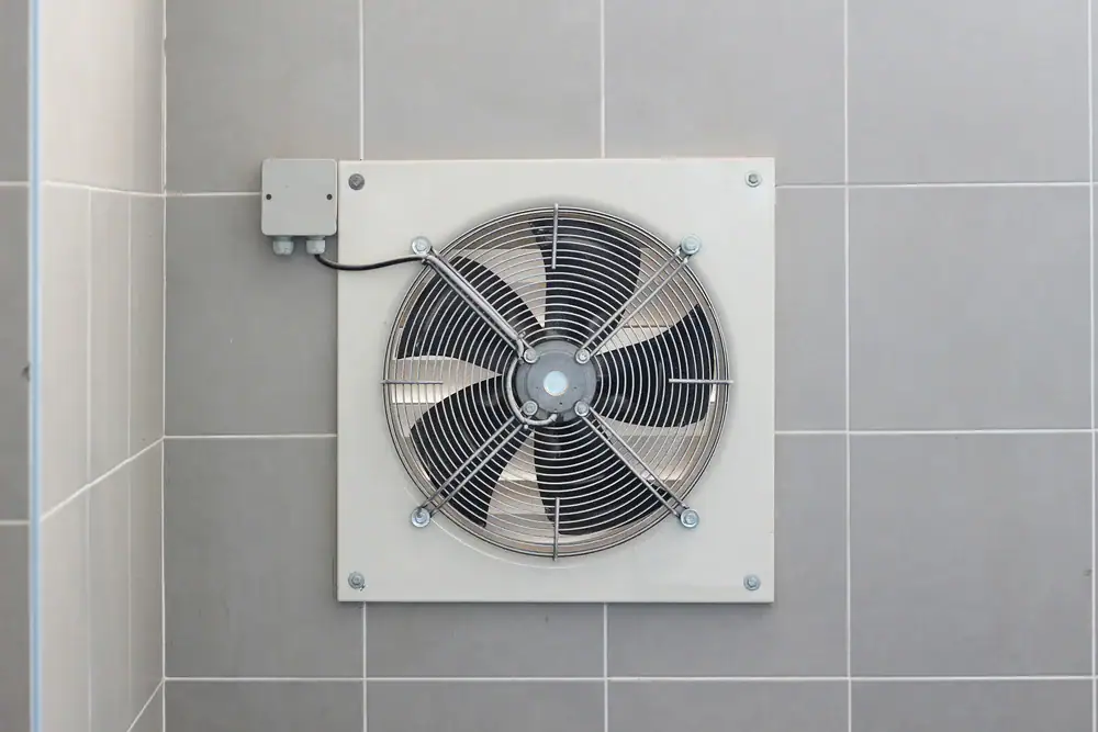 A wall-mounted exhaust fan with a protective grille is installed on a tiled wall, helping with ventilation in the room.